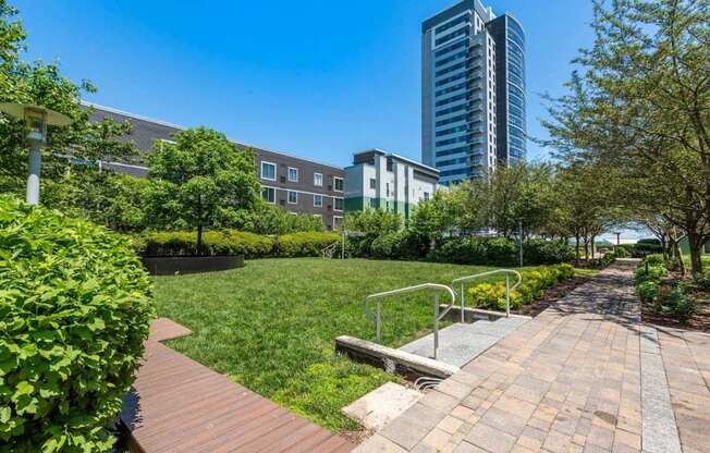 A park with a wooden walkway and a bench in the foreground with a cityscape in the background.