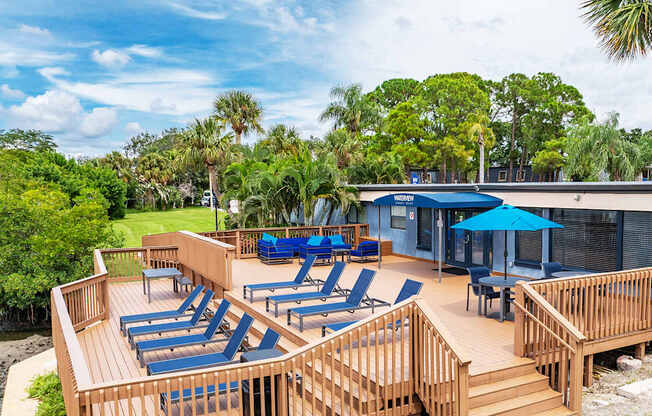 A wooden deck with blue lounge chairs and a blue umbrella.