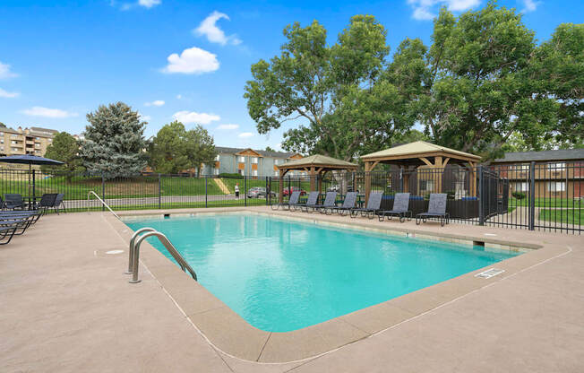 A swimming pool surrounded by a black fence and trees at Mountain Vista Apartments, Lakewood, 80228