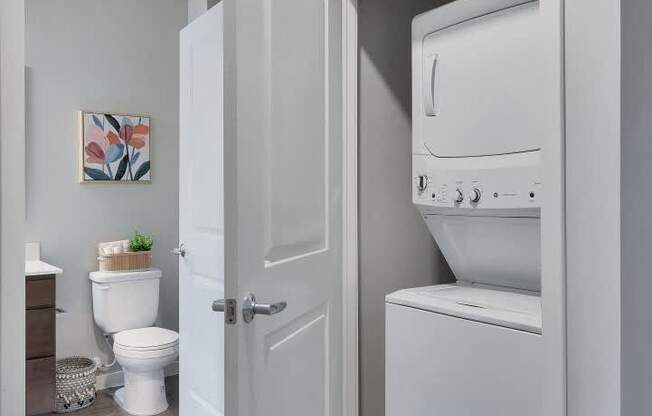 A white door opens to a bathroom with a toilet and a washing machine.