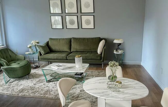 A living room with a green couch, white chairs, and a glass table.