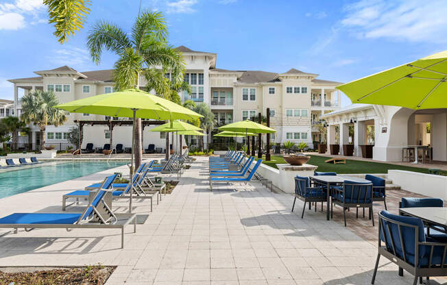 a pool with blue chairs and yellow umbrellas and buildings in the background