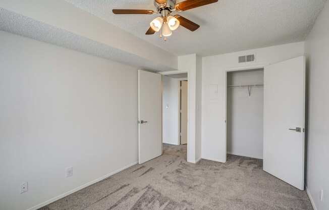 an empty bedroom with a ceiling fan and a closet