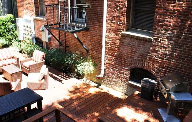 Brookmore Pasadena ca apartments back patio surrounded by greenery and brick wall with wicker patio furniture, stained wood deck, and grilling station.