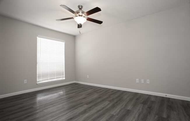 an empty living room with a ceiling fan and a window