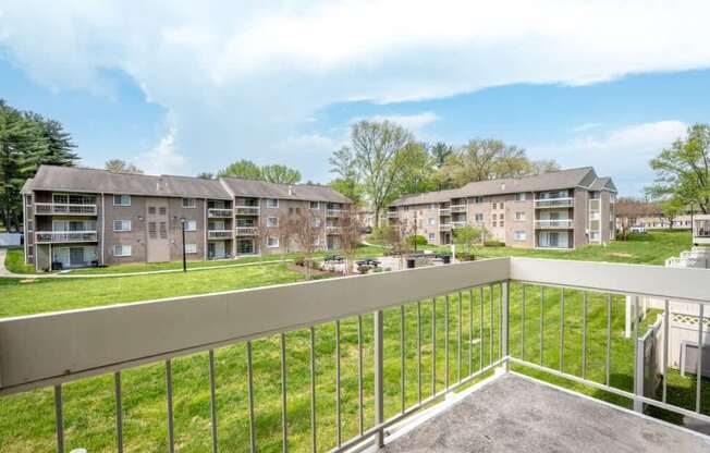 A balcony overlooks a grassy area with apartment buildings in the distance.