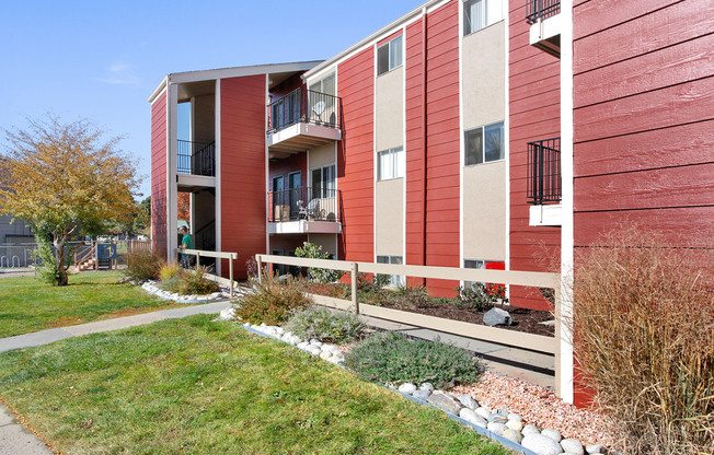 Charming red apartment building with balconies, surrounded by lush landscaping and a peaceful walkway.
