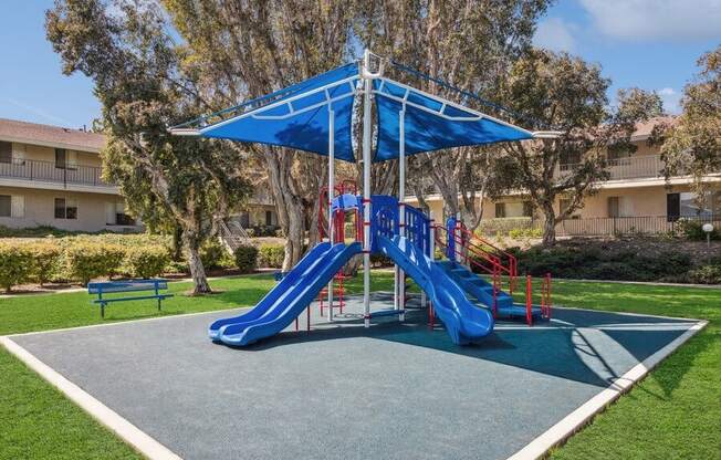 Community Playground with Two Slides and a Blue Canopy at Forest Park Apartments in El Cajon, CA.