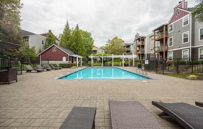 A pool surrounded by a black fence and a red barn.