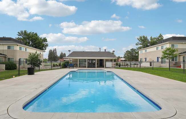 A large outdoor swimming pool surrounded by a concrete patio and a black fence.