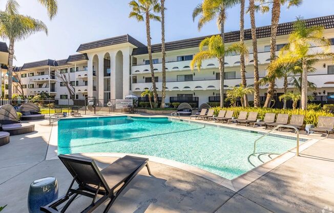 A pool surrounded by palm trees and lounge chairs.