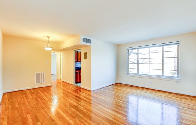vacant living area with large windows, hard wood flooring and  view of kitchen in cambridge square apartments in bethesda md