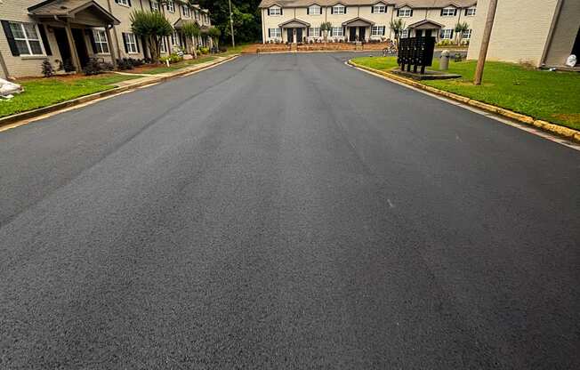 A street view of a residential area with houses on the left and a road on the right.