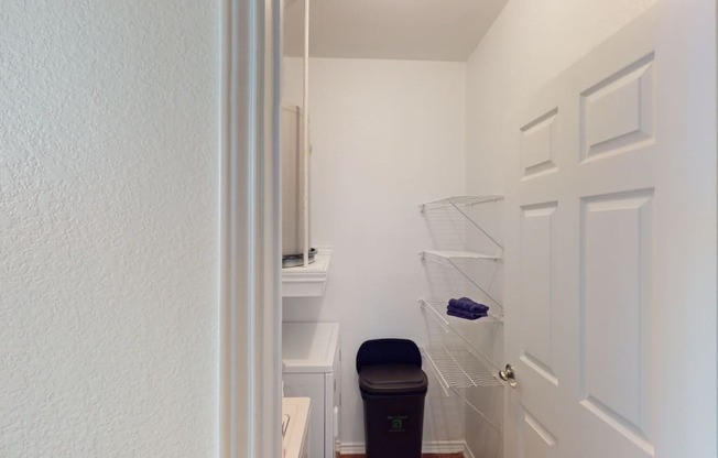 a small closet in a bathroom with a trash can and a white door