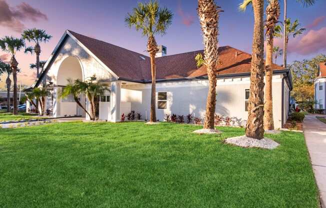 the front of a house with palm trees and grass