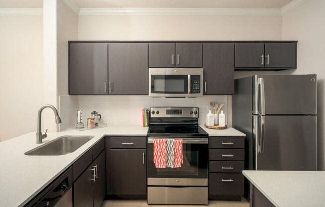 Model kitchen with dark brown cabinets, white quartz countertops, and stainless steel appliances