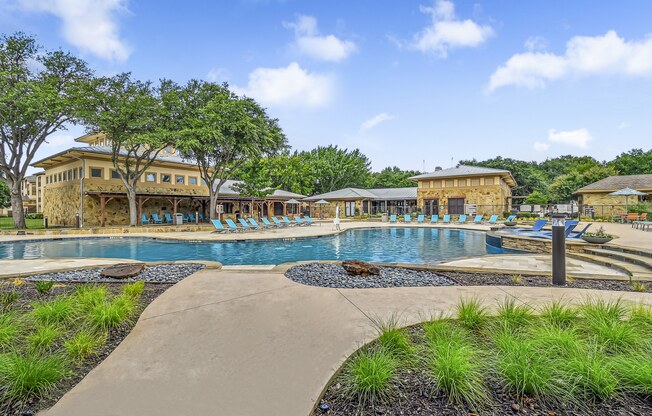 A large outdoor swimming pool surrounded by trees and lounge chairs. at The Canyons Apartments, Fort Worth, TX