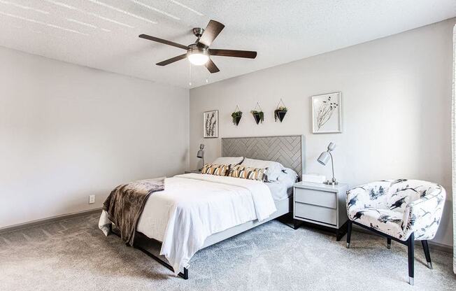 A bedroom with a bed, chair, and ceiling fan.