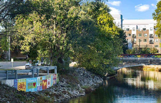 A river flows under a bridge with a colorful mural on the side.