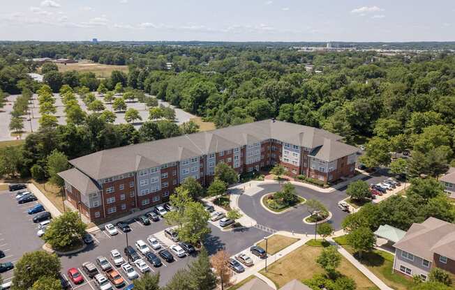 an aerial view of a large brick building with a gray roof and a parking lot with cars