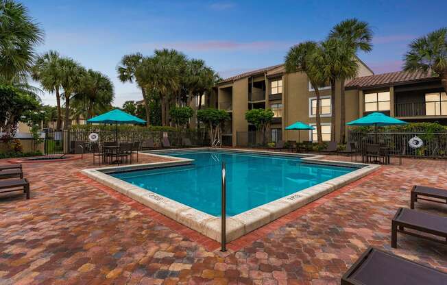 A pool surrounded by a brick patio and palm trees.