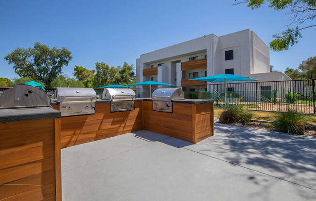 two bbq grills with umbrellas and a building in the background