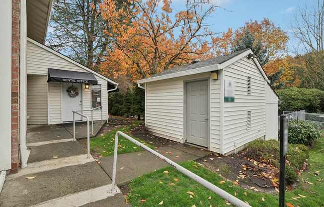 A small white building with a sign that says "RENTAL OFFICE" is in front of a tree with orange leaves.