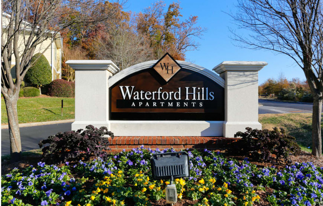 a sign for waterford hills apartments in front of a flower garden