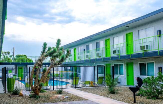 Fusion Las Vegas apartment buildings with lime green doors flanking community pool and courtyard with desert landscaping and barbecue.