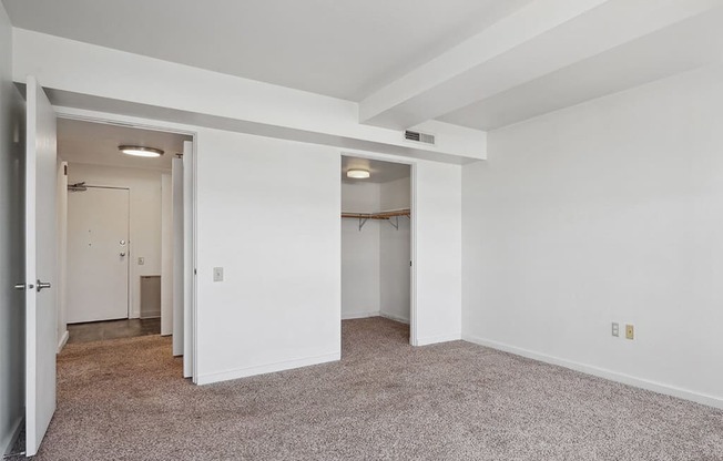 a bedroom with white walls and carpet and a door to a closet