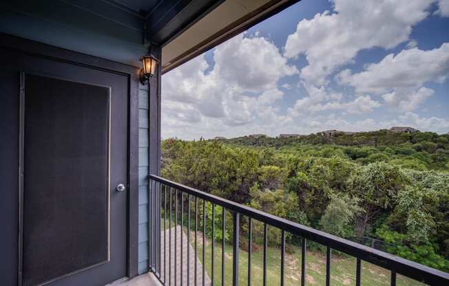 a balcony with a door and a view of trees and a cloudy sky