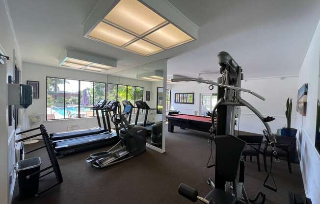 a gym with exercise equipment and windows with a pool