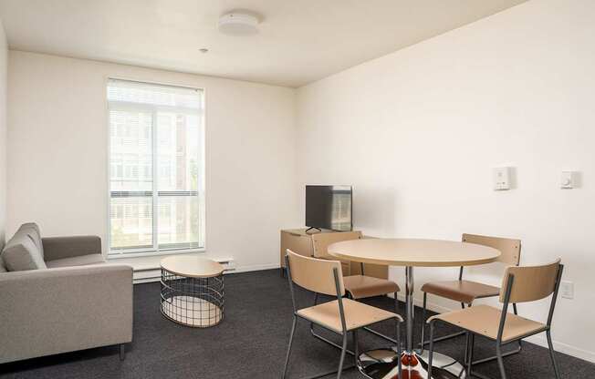 A living room with a grey couch, a round table with four chairs, and a television.