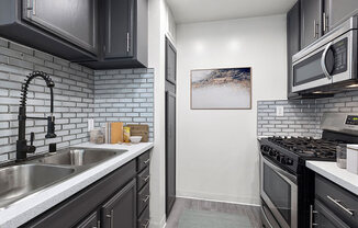 White tiled kitchen with stainless steel fridge, oven, microwave, and fixtures.