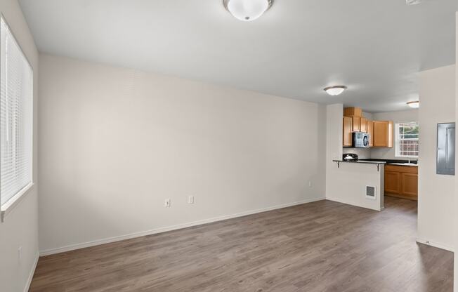 an empty living room and kitchen with wood flooring and white walls