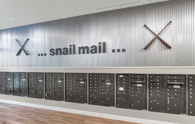 A row of black mailboxes are lined up against a wall with a Snail mail sign above them.