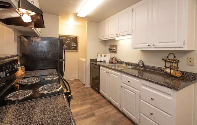 A kitchen with a black stove top oven and white cabinets at Bishop's Court Apartments, California, 95670