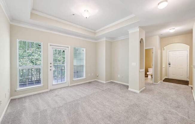 A spacious living room with vaulted ceilings,  a carpeted floor, large windows,  and a artwork niches.