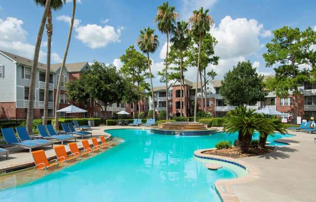 a large swimming pool with orange chairs in front of apartment buildings at Veranda at Centerfield, Texas