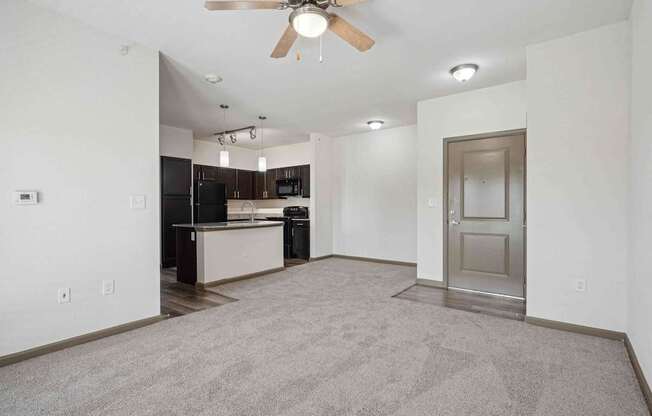 Apartments for Rent in Bentonville, AR 72713– Parc at Bentonville -   A spacious living room with a ceiling fan and a kitchen in the background.
