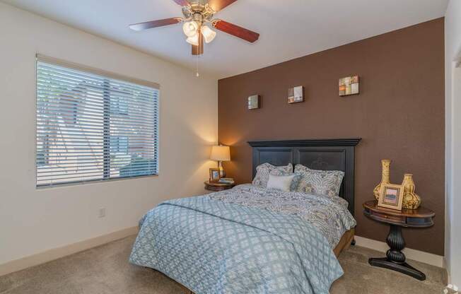 A bedroom with a bed, a ceiling fan, and a window with blinds.