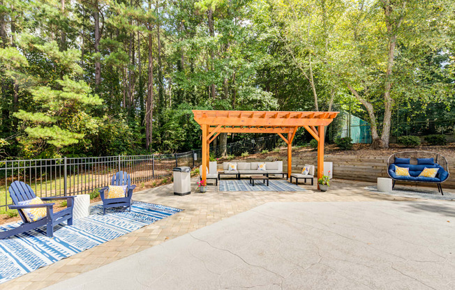 A wooden pergola is in the middle of a concrete patio with chairs at Laurel Oaks in Raleigh, NC.