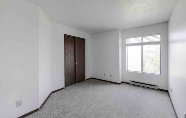 A room with a carpeted floor, a window with blinds, and a door.