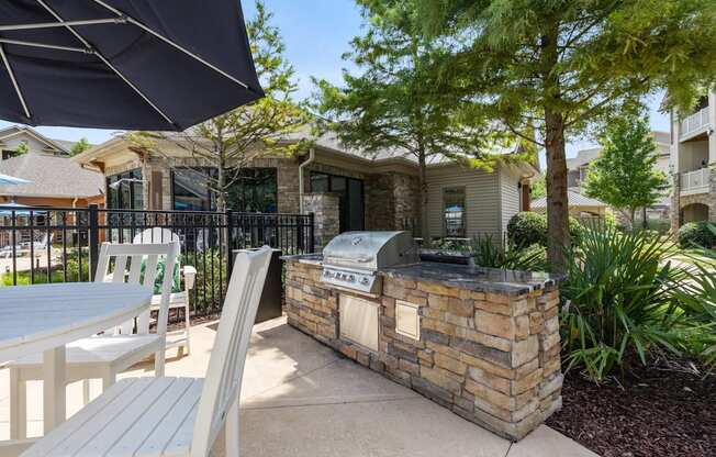 A patio with a grill and chairs under a black umbrella.