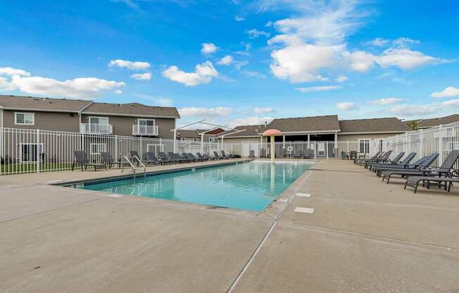 A large swimming pool surrounded by lounge chairs and apartment buildings.