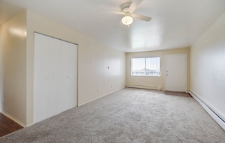 Bright and welcoming living space with plush carpeting, large window, and ceiling fan, perfect for relaxation.