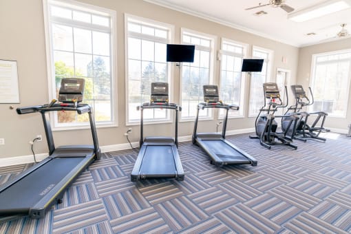 a fitness room with cardio machines and windows