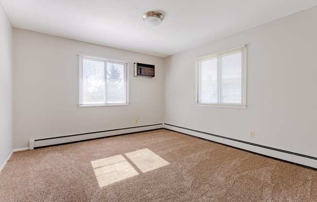 an empty living room with carpet and two windows