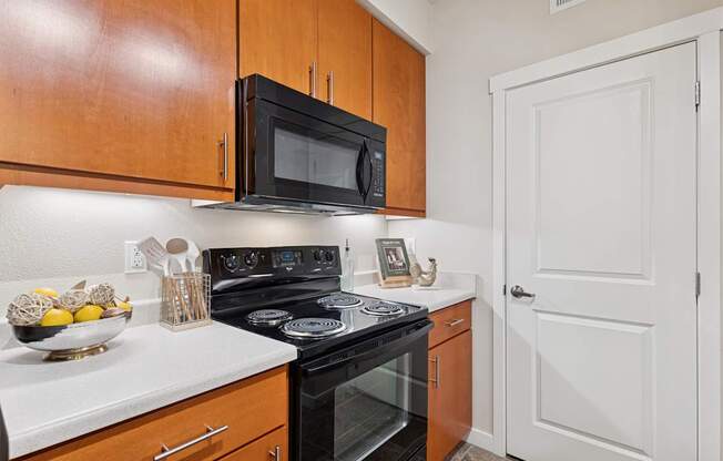 A kitchen with a black microwave above a stove and wooden cabinets.