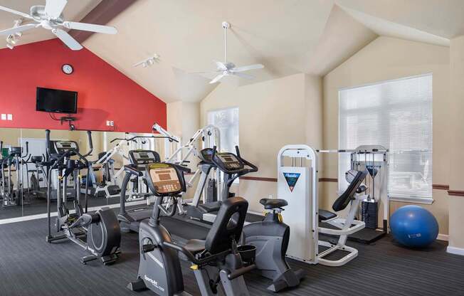 a gym with cardio equipment and a red wall